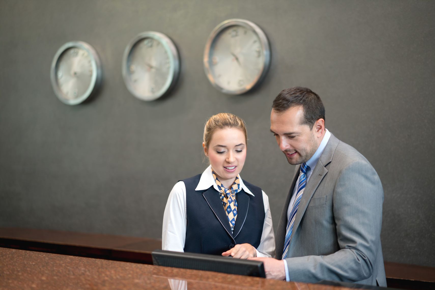 Two people looking at somethin gwith 3 clocks in background